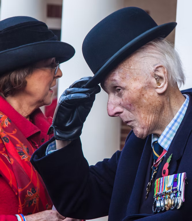 A veteran in a bowler hat greeting a woman during the Remembrance Day service